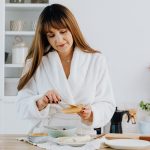 A woman in a bathrobe preparing breakfast in a home kitchen.